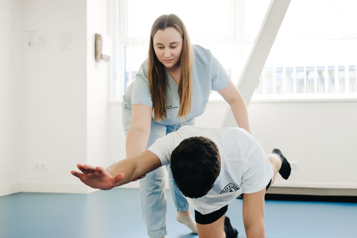 Fisioterapeuta auxiliando um paciente em um exercício de alongamento em uma sala clara.
